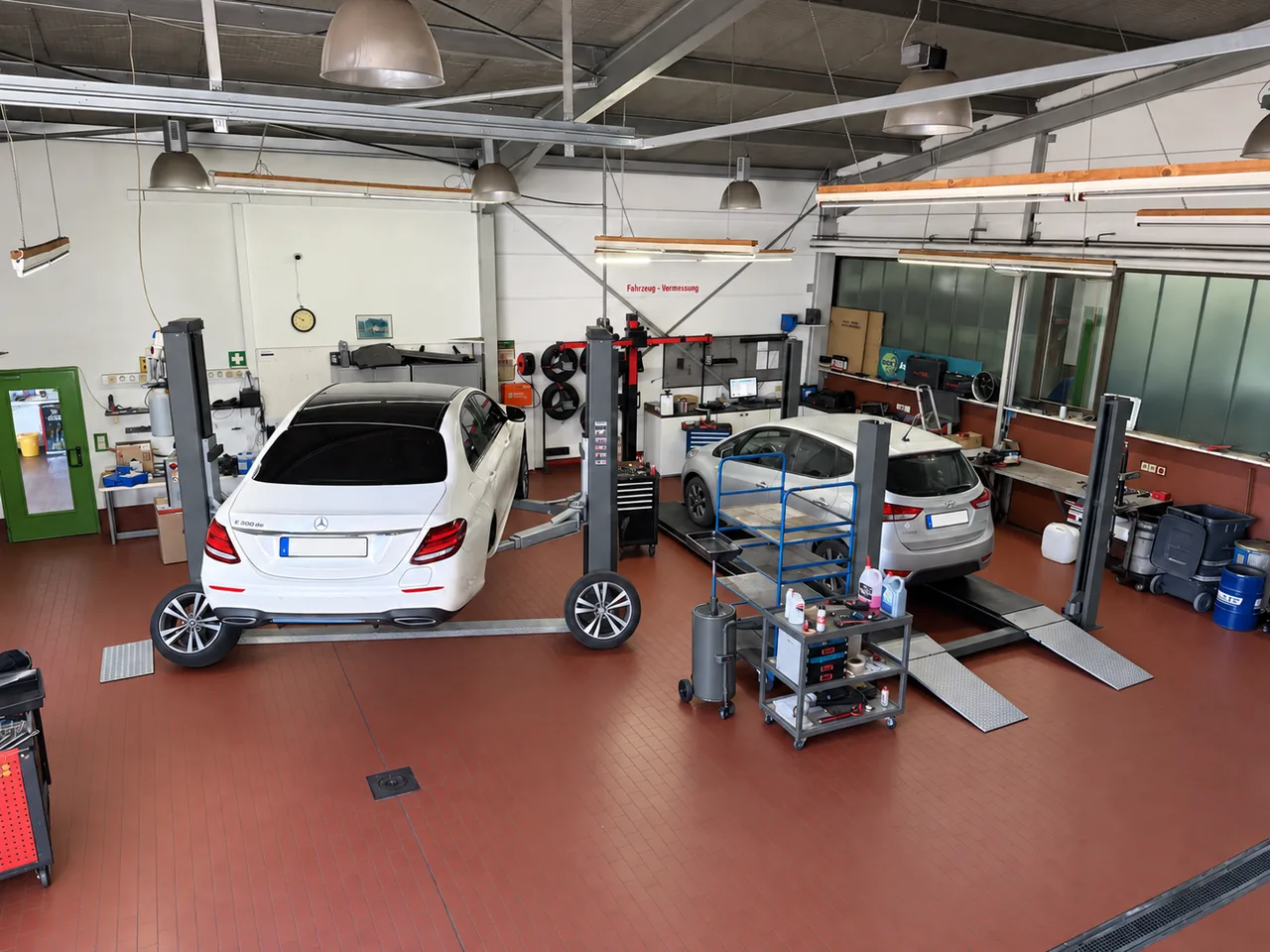 Werkstatthalle des Autozentrums Kozak mit zwei Fahrzeugen auf Hebebühnen, Werkzeugwagen und Prüfgeräten