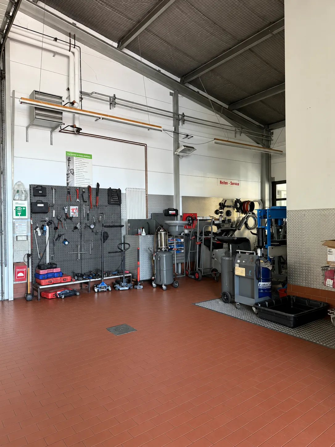 Arbeitsbereich der Werkstatt mit Geräten, Werkzeugwand und Wagen an der Hallenwand