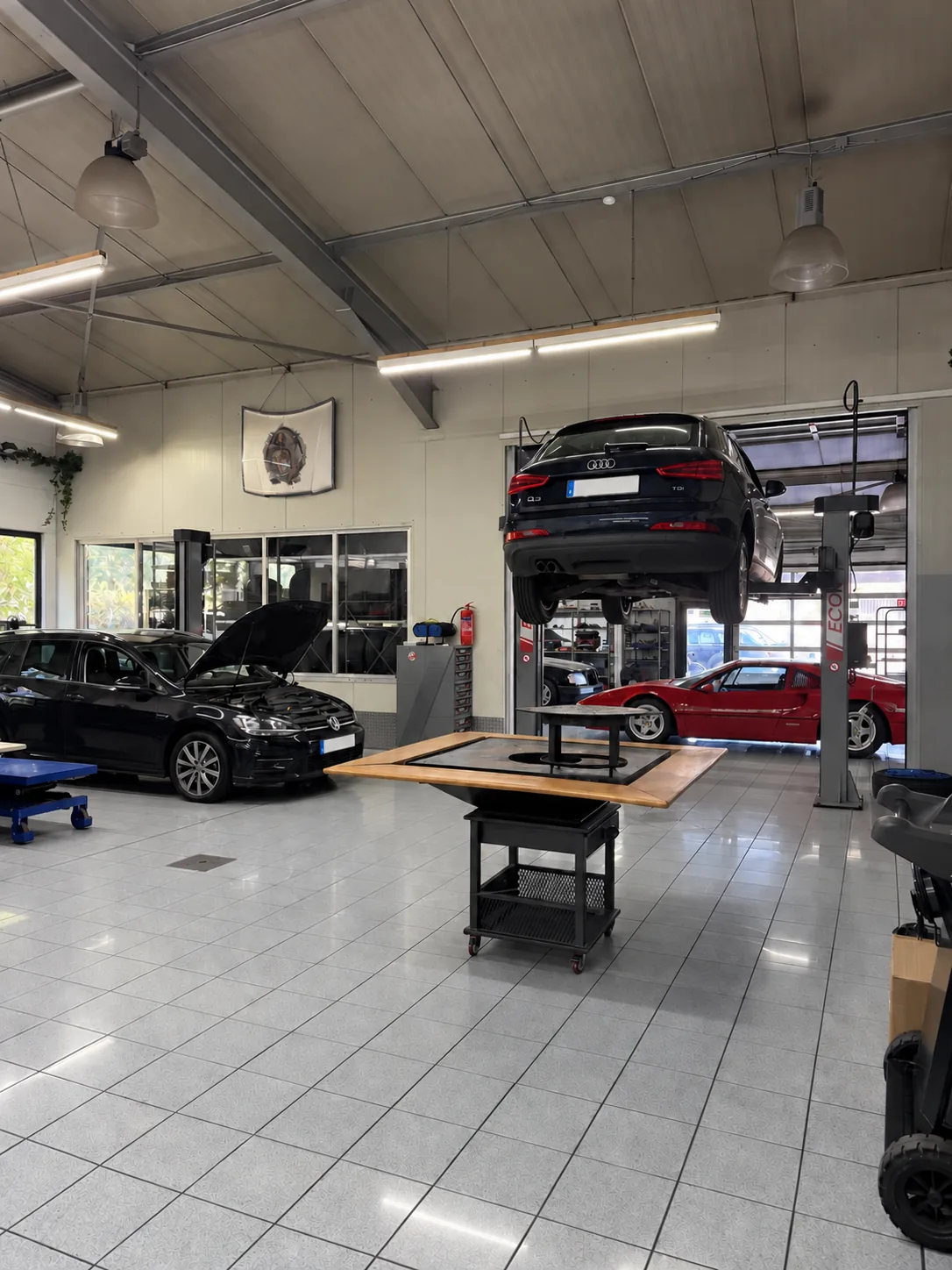 Werkstatthalle mit einem Fahrzeug auf der Hebebühne, dahinter weitere Fahrzeuge in Arbeit